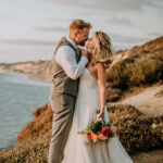 husband kissing wife romatically on wedding day on a golden california cliffside