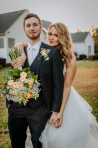 BRIDE WITH HER ARM HANGING ON HUSBAND'S SHOULDERS WITH BOQUET IN HAND